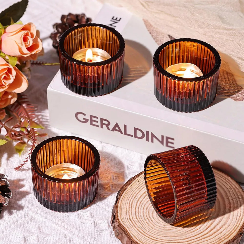 A collection of amber glass tealight candle holders displayed on a white box and natural wood surface.