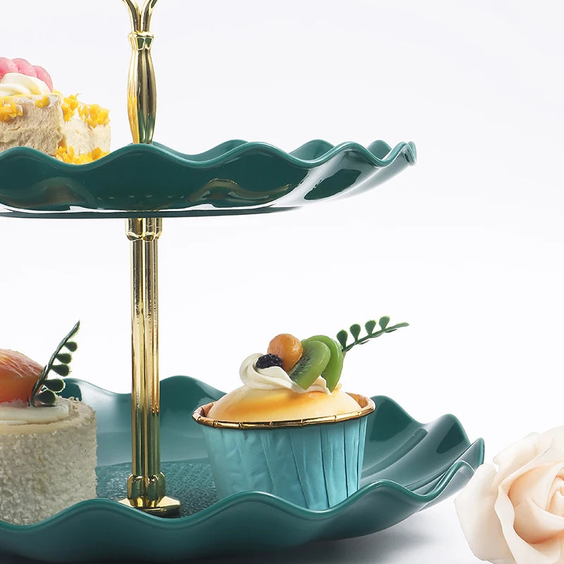 A two-tier serving stand in teal ceramic with a gold pedestal holding desserts and fruit.