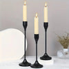 A set of three black candle holders with white candles on a white surface.