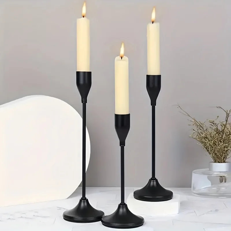 A set of three black candle holders with white candles on a white surface.