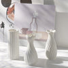 White ceramic bud vase with vertical ridges displayed in front of a framed artwork.