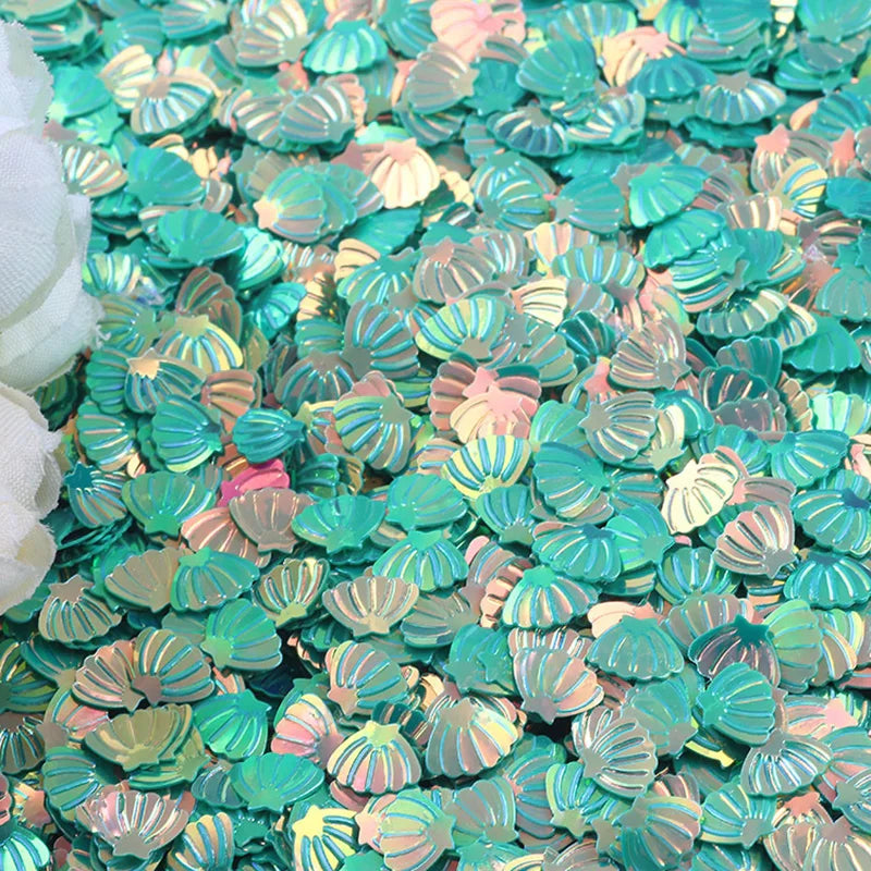 A pile of iridescent teal and pink seashell-shaped confetti or sequins for a party decoration.