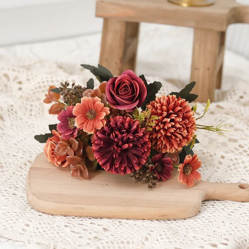 A bouquet of silk autumn roses and hydrangea flowers arranged on a wooden cutting board.