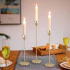 A set of three elegant gold metal candle holders with white candles displayed on a wooden table.