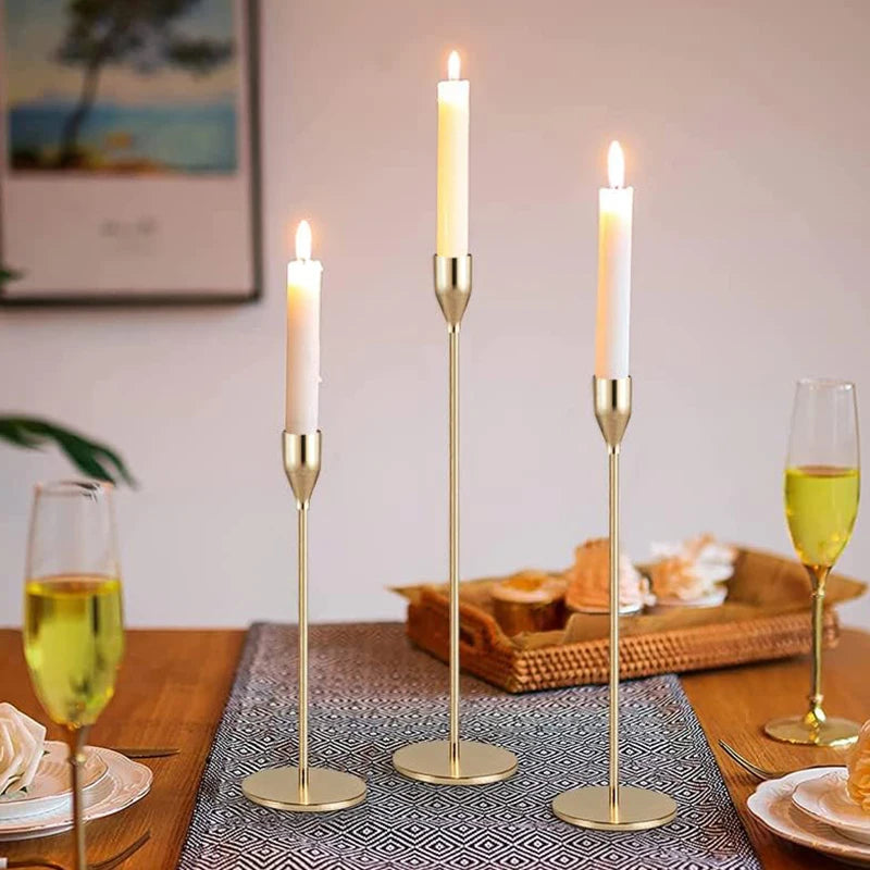 A set of three elegant gold metal candle holders with white candles displayed on a wooden table.