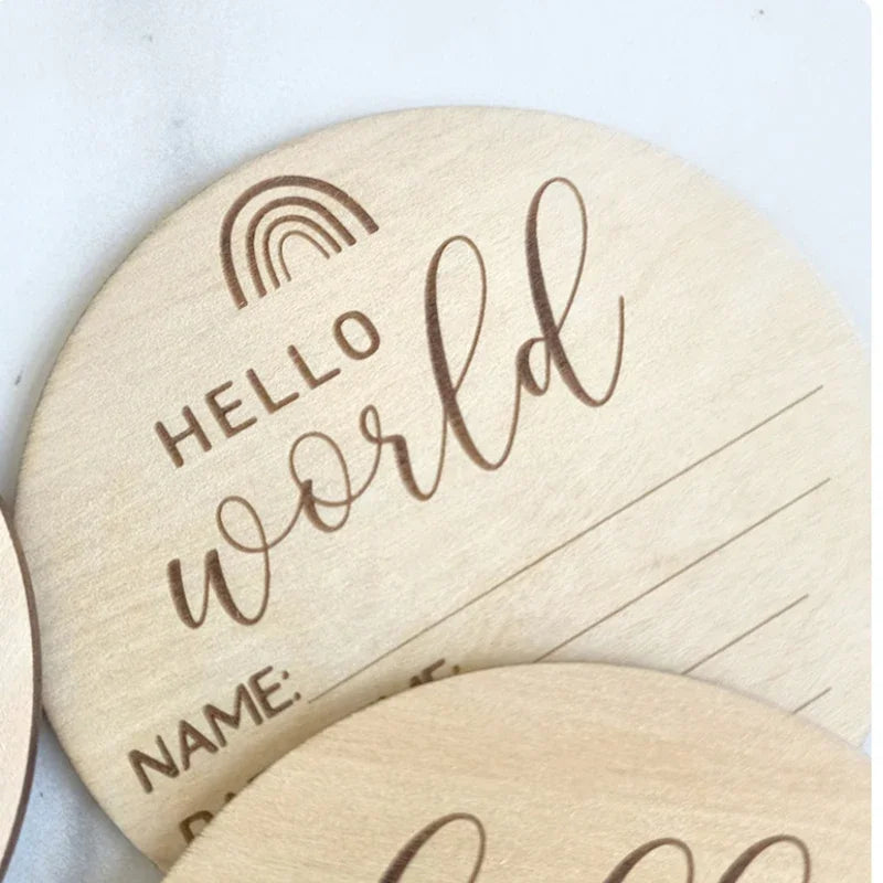 A round natural wood baby milestone disc with the words hello world and a rainbow design.