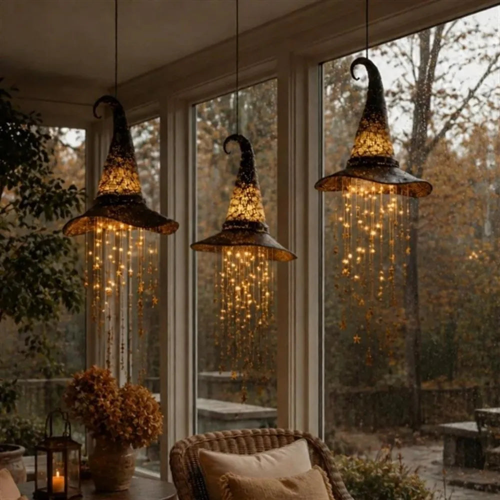 A glowing witch hat hanging chime with star tassels suspended in a window frame.