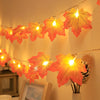 An autumn leaf garland with LED lights is displayed against a light wall, featuring orange and yellow tones.