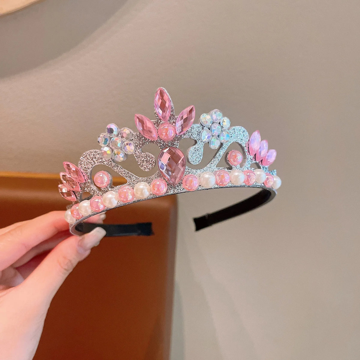 A set of three sparkling pink and iridescent pearl headbands displayed on a hand.