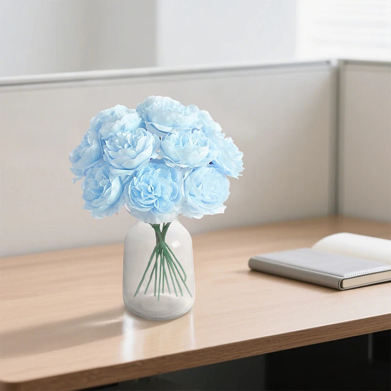 A small vase holds a bouquet of six light blue peony flowers on a wooden desk.