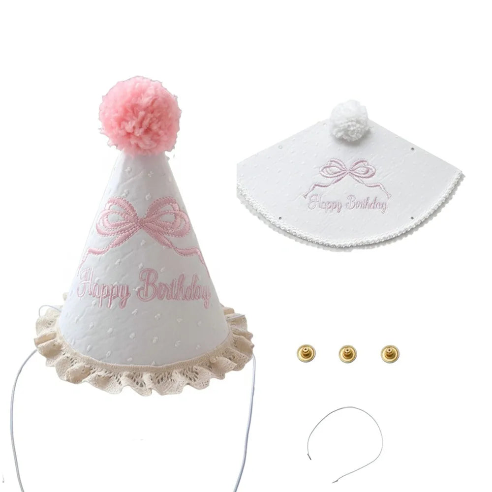 A white conical birthday hat with pink pompom and ribbon details, along with small gold ear loops.