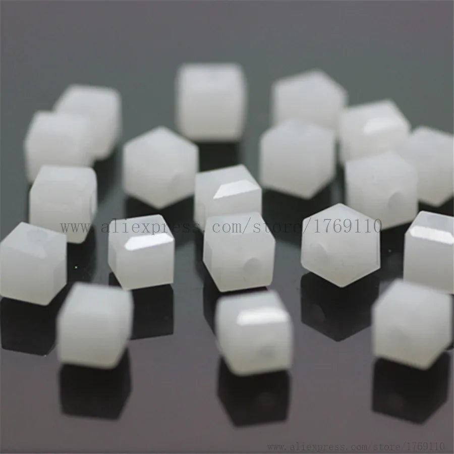 A collection of white square cut glass crystal beads scattered on a dark surface.