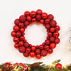 A wreath made of shiny red and bronze glitter Christmas balls on a green branch with lights.