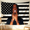 A man with dreadlocks looks directly at the camera against an American flag backdrop featuring stars and stripes.