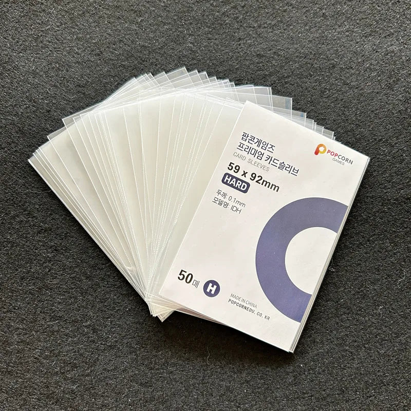 A stack of 50 clear hard card sleeves for trading cards is displayed on a dark gray surface.