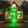 A green inflatable alien decoration with glowing eyes stands in front of a wooden house during sunset.