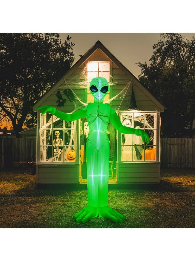 A green inflatable alien decoration with glowing eyes stands in front of a wooden house during sunset.