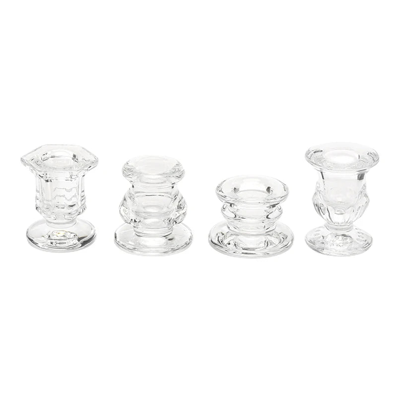 A set of four clear glass candle holders or candlesticks with decorative bases.