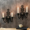 A vintage black wall pendant candle holder mounted on a gray wall above a wooden surface.