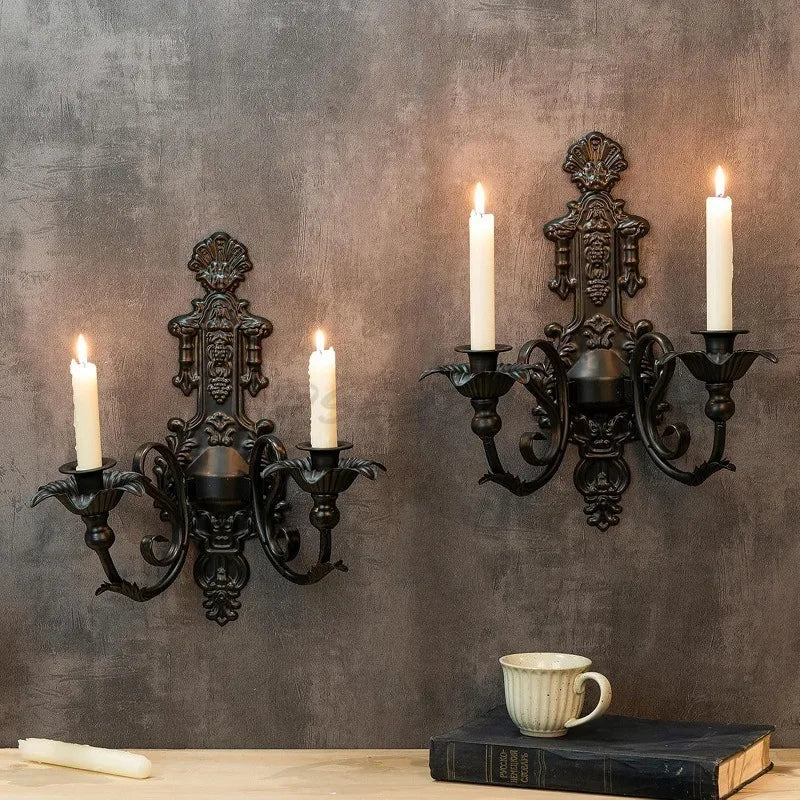 A vintage black wall pendant candle holder mounted on a gray wall above a wooden surface.