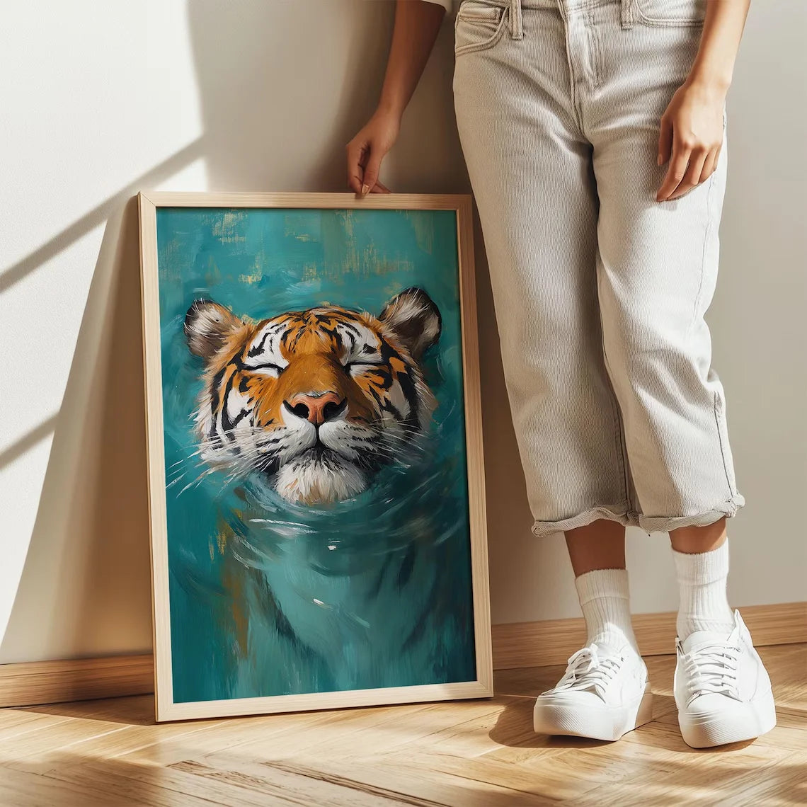 A person stands next to a framed painting of a tiger underwater on a light-colored wall.