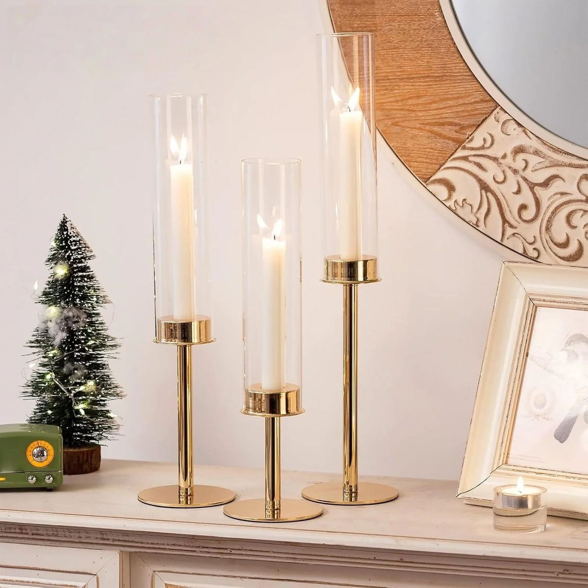 A set of three tall glass hurricane candle holders with gold accents displayed on a white surface.