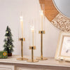A set of three tall glass hurricane candle holders with gold accents displayed on a white surface.