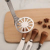 A silver manual potato and pumpkin masher is shown resting on a wooden cutting board with several wooden tools.