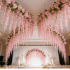 A lavish wedding ceremony setup featuring a pink silk wisteria hanging vine garland draped across the ceiling.