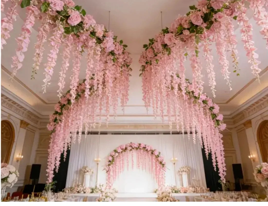 A lavish wedding ceremony setup featuring a pink silk wisteria hanging vine garland draped across the ceiling.