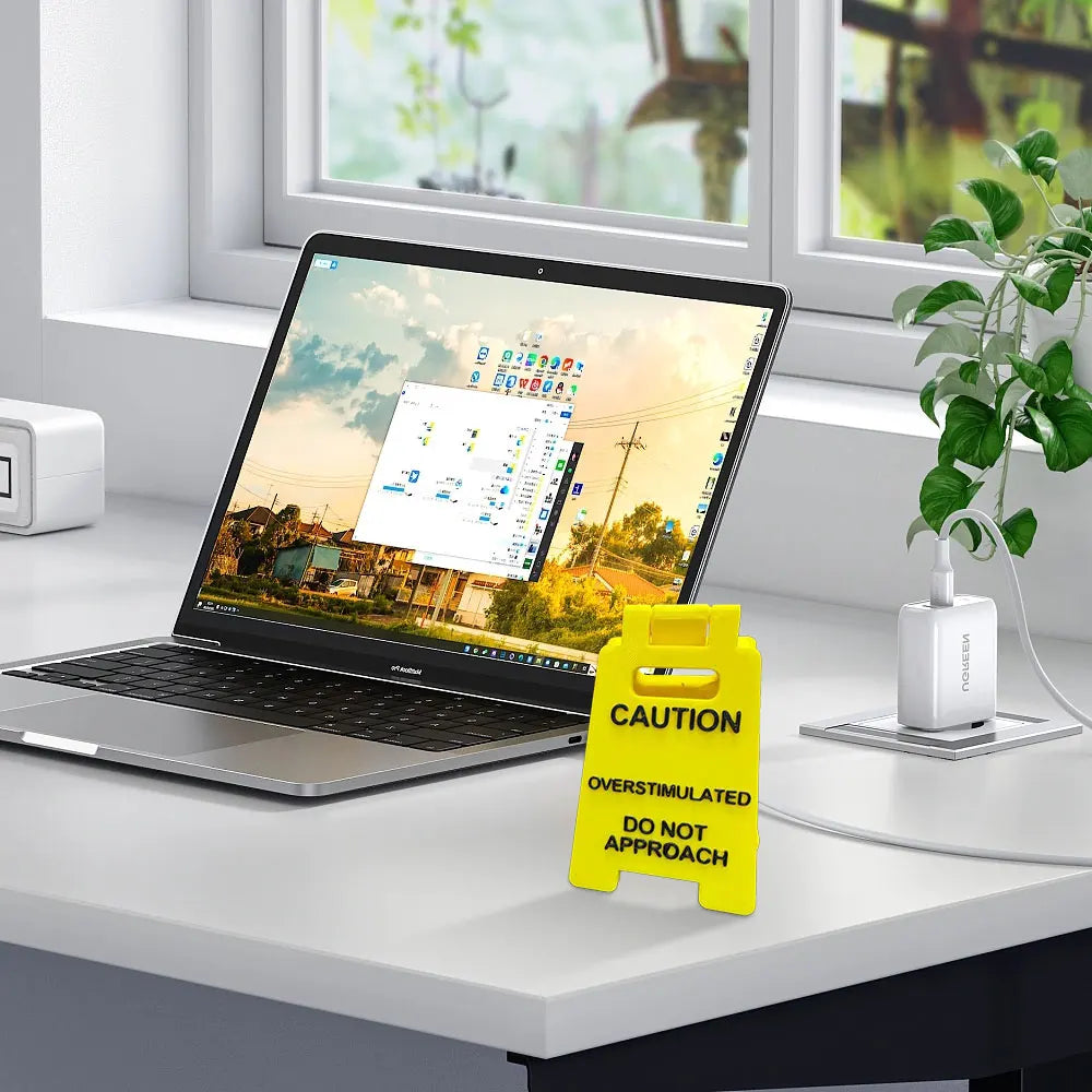 A yellow caution sign for overstimulated days rests on a desk in front of a laptop.