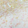 A close-up view of iridescent pink and yellow sea shell PVC sequins scattered on a light surface.
