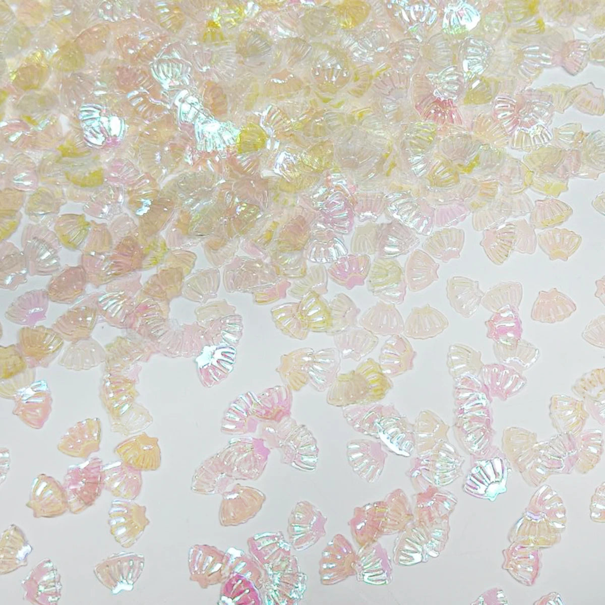 A close-up view of iridescent pink and yellow sea shell PVC sequins scattered on a light surface.