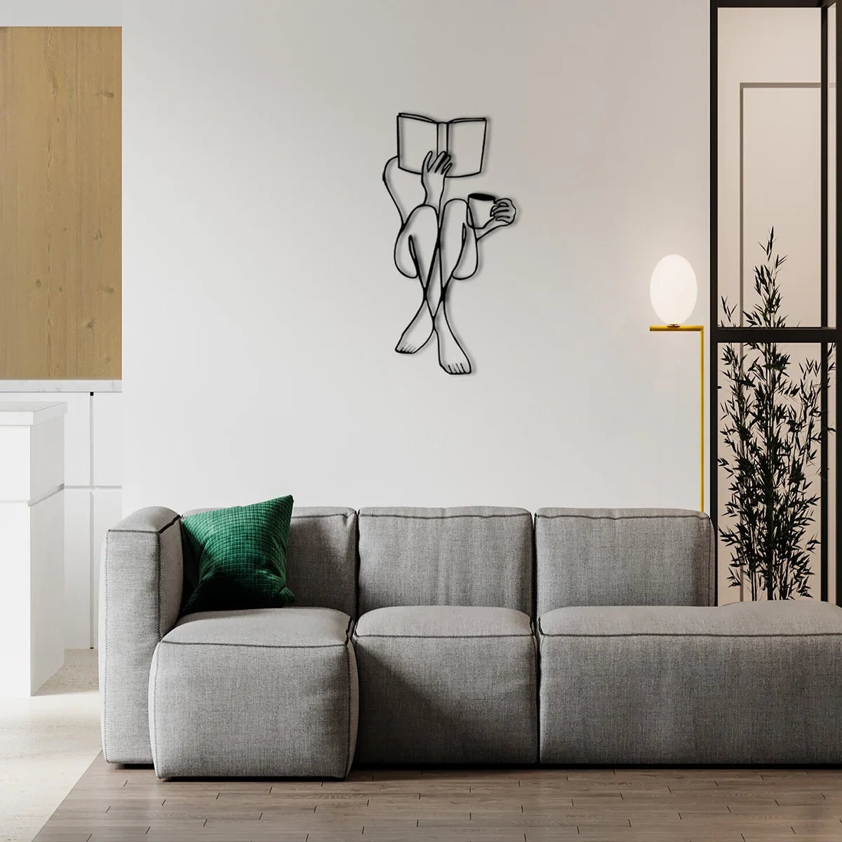 A modern gray sofa is positioned in front of a white wall featuring an elegant metal line art sculpture of two figures.