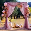 Un tissu en mousseline rose drapé forme une arche élégante pour un événement extérieur.
