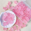 A clear plastic container filled with pink glow-in-the-dark resin pig decorations and loose pieces on a white surface.