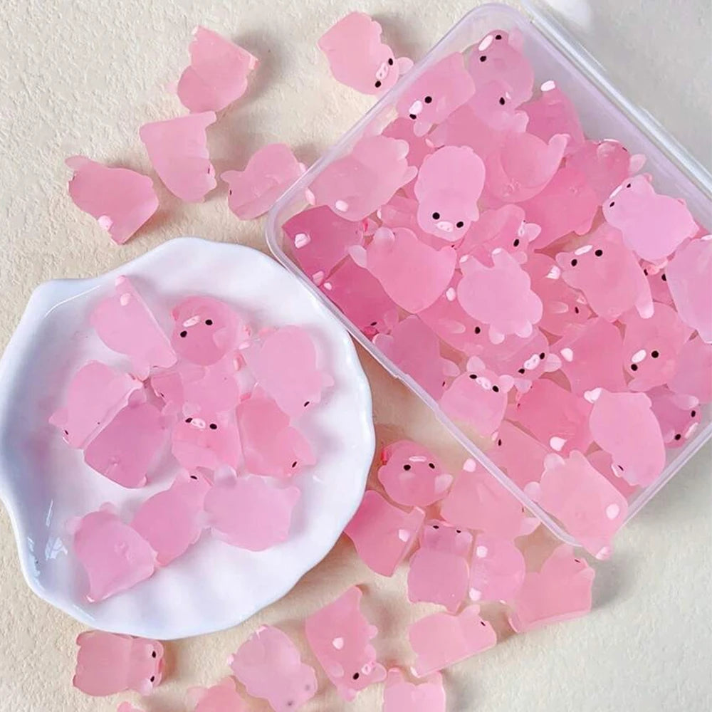 A clear plastic container filled with pink glow-in-the-dark resin pig decorations and loose pieces on a white surface.