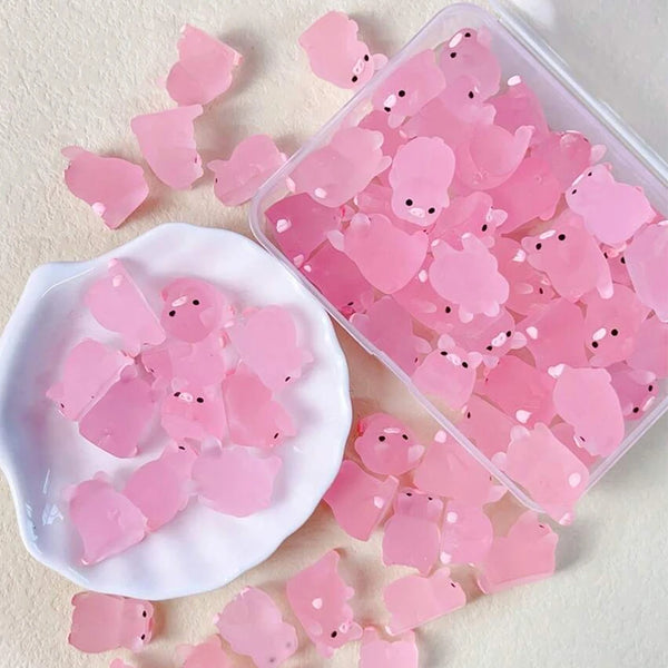A clear plastic container filled with pink glow-in-the-dark resin pig decorations and loose pieces on a white surface.