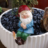 Keramiks statue eines bärtigen Gnomens mit rotem Hut und blauer Kleidung, der mit einer grünen Angelrute in eine Schale mit s