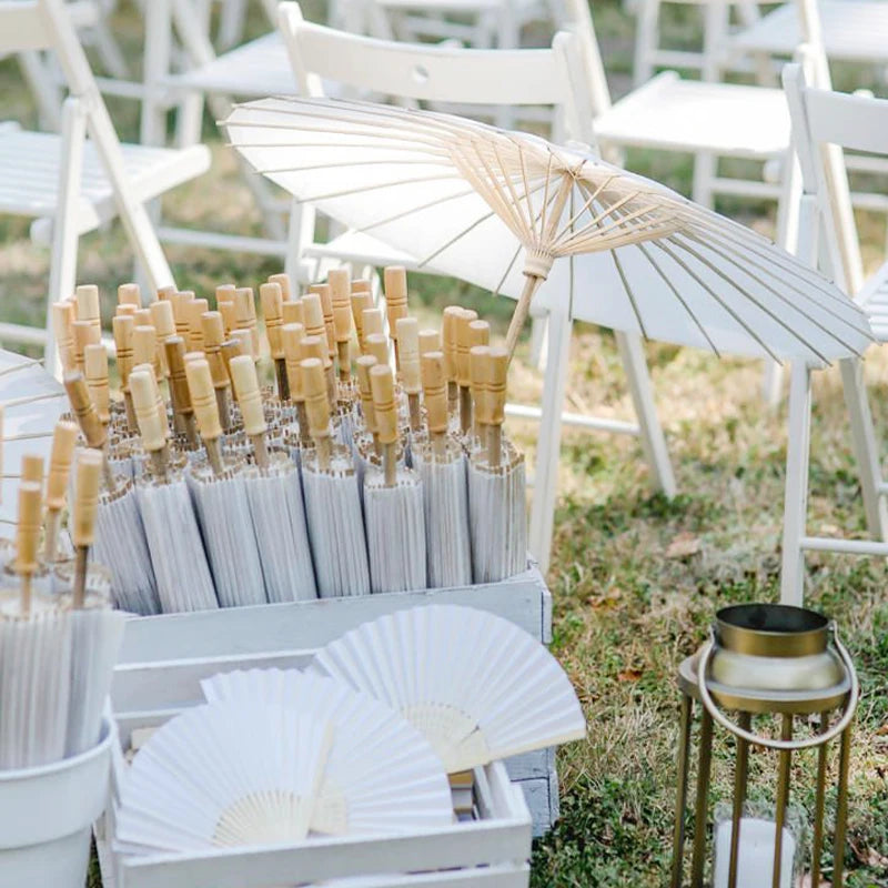 A display of handcrafted white oil paper umbrellas and wooden straws set up outdoors for wedding decor.