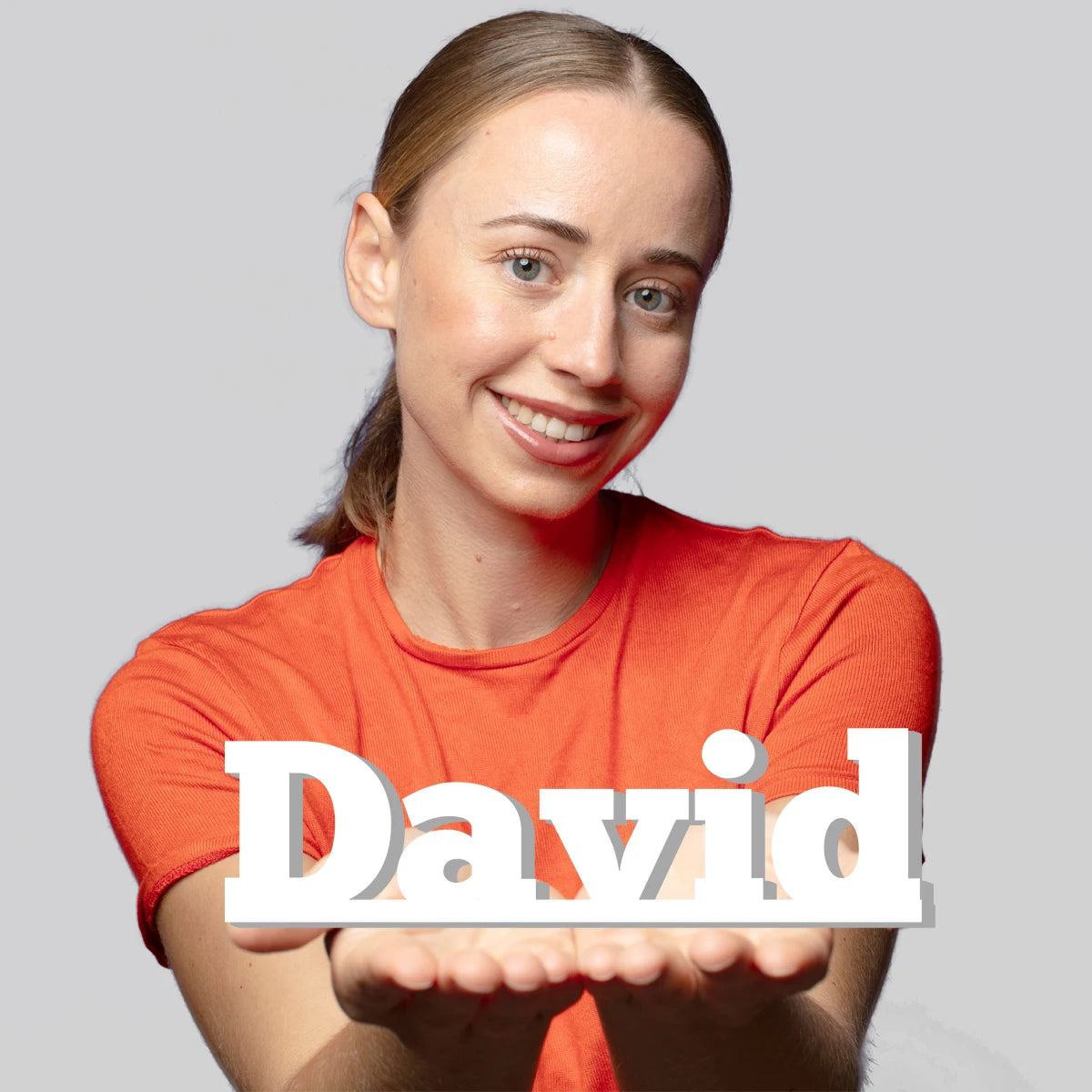 A smiling young woman with light hair wearing an orange shirt is presenting her hands forward.