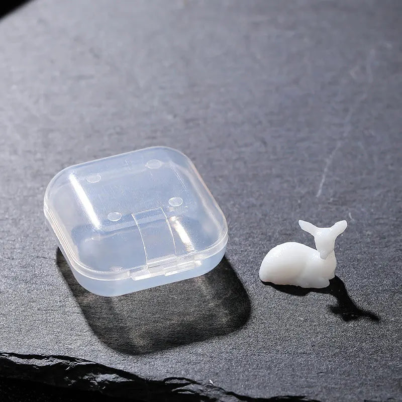 A clear plastic container holds a white resin ornament shaped like an elk or deer.