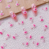 Una colección de 50 aderezos de uñas en forma de tortuga mini rosa y blanco esparcidos sobre una superficie blanca texturizad