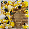 A yellow and gold balloon arch wreath set decorated with black and white balloons, featuring a wicker chair in the background