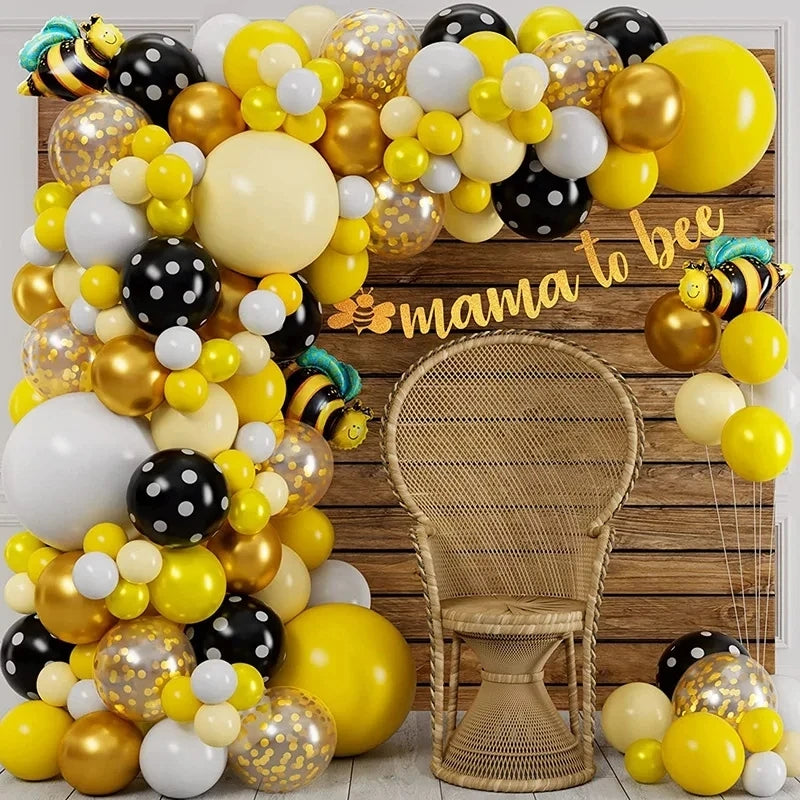 A yellow and gold balloon arch wreath set decorated with black and white balloons, featuring a wicker chair in the background