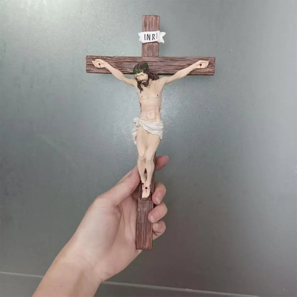 A hand holds a small, hand-painted resin cross statue depicting Jesus Christ on a wooden cross.