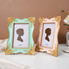 A pair of ornate, gold-framed photo frames with light mint green and blush pink backgrounds displaying silhouette portraits.