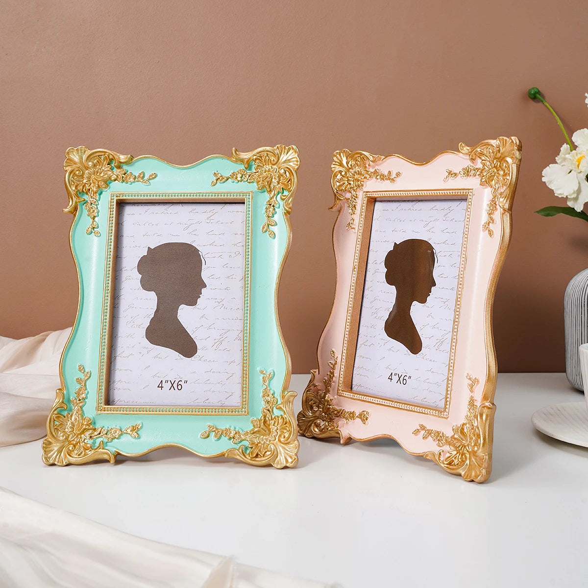 A pair of ornate, gold-framed photo frames with light mint green and blush pink backgrounds displaying silhouette portraits.