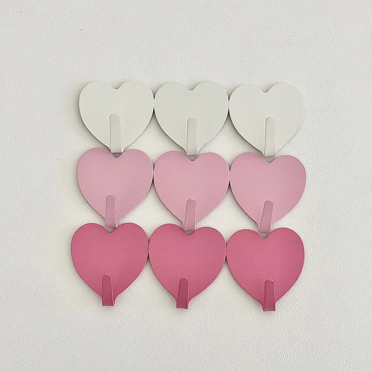 A set of six heart-shaped adhesive hooks in white and pink for use as no-drill key hooks.