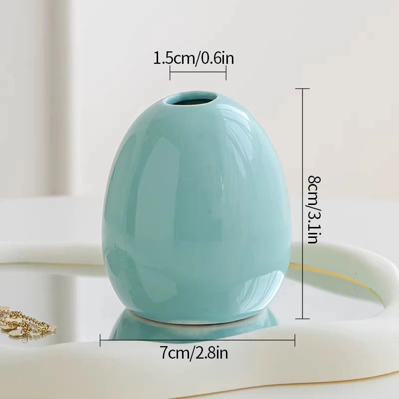 A light blue ceramic mini vase with a smooth finish is shown on a white surface.